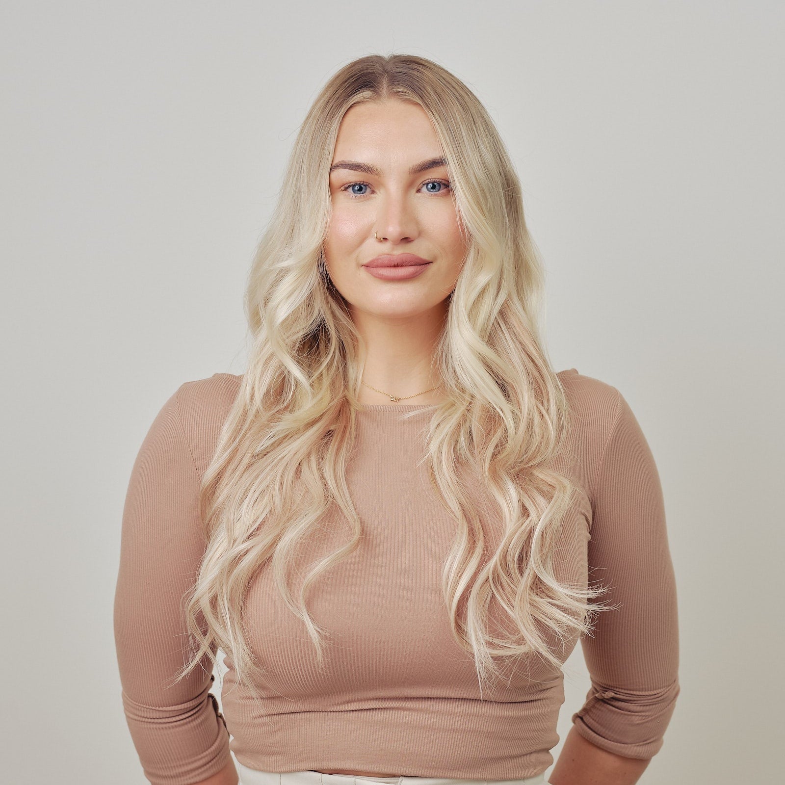 Woman with long blonde hair clip in hair extensions against a plain background